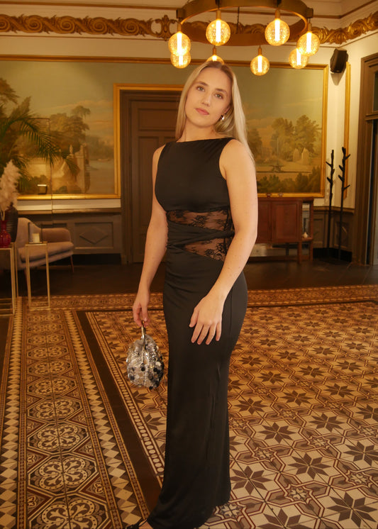 Woman in a black dress standing in an elegant room with chandelier and paintings.